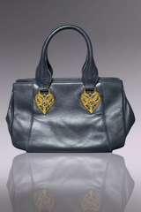 Black handbag with gold heart-shaped embellishments on a reflective surface