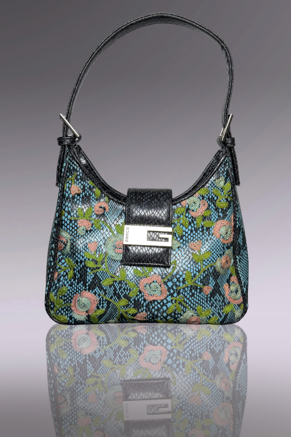 Floral patterned handbag with a black strap on a reflective surface