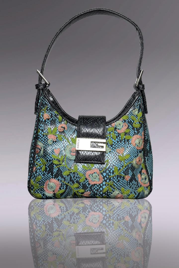 Floral patterned handbag with a black strap on a reflective surface