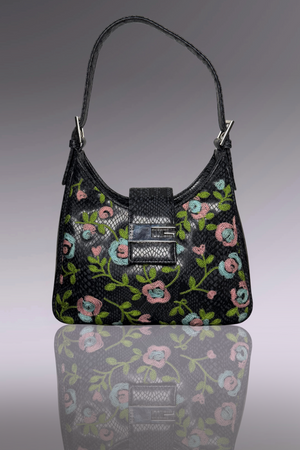 Black handbag with floral embroidery on a reflective surface