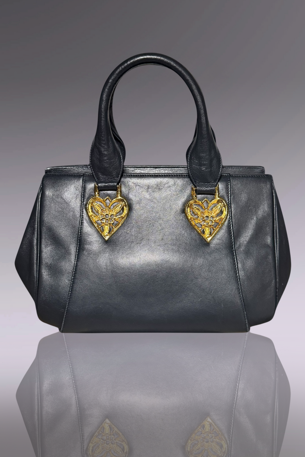 Gray handbag with gold heart-shaped embellishments on a reflective surface