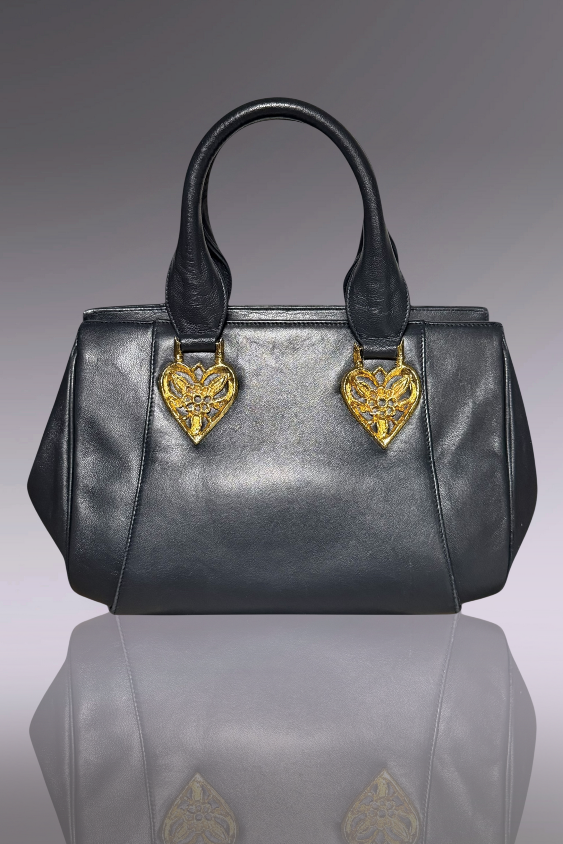 Gray handbag with gold heart-shaped embellishments on a reflective surface