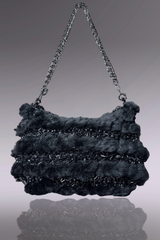 Black textured handbag with chain handle on a reflective surface
