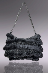 Textured handbag with chain strap on a reflective surface
