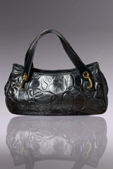 Black embossed handbag on a reflective surface with a gray background