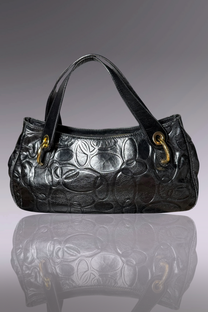 Black embossed handbag on a reflective surface with a gray background