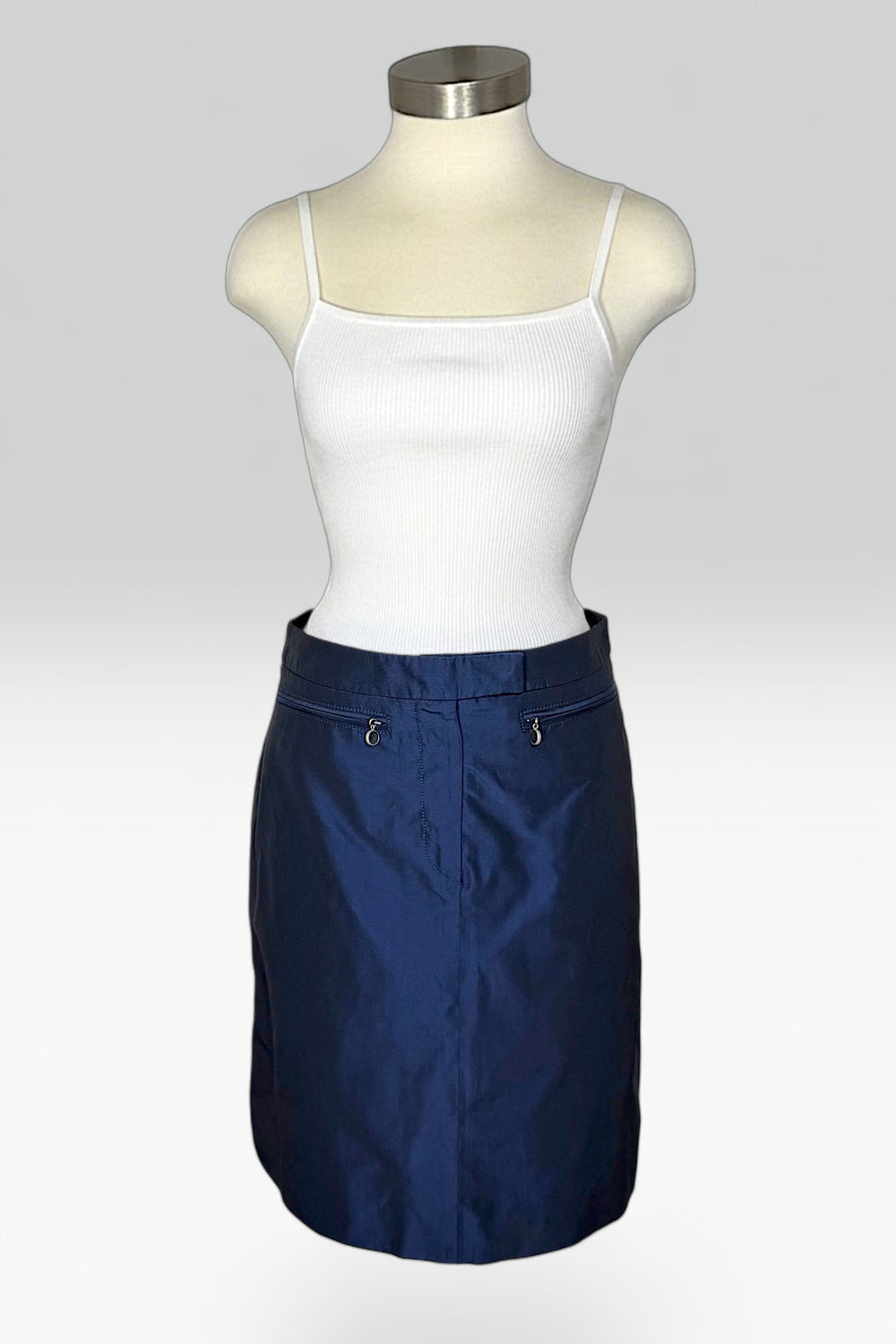 A navy blue mini skirt displayed on a mannequin torso, styled with a white ribbed camisole top against a light gray studio background.